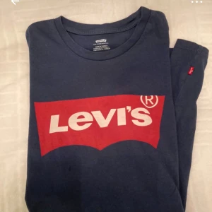 Blå Levi's t-shirt med röd logga - Snygg blå t-shirt från Levi's med den klassiska röda loggan tryckt på bröstet. T-shirten har rund halsringning och är kortärmad. Tillverkad i mjuk bomull som är skön att ha på sig hela dagen.