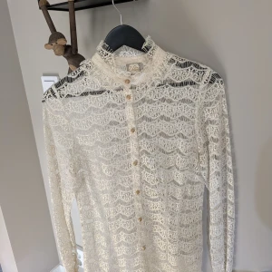 Vit spetsblus med guldknappar Vintage - Superfin cremeförgad spetsblus med dekorativa guldiga knappar. Blusen har ett genombrutet spetsmönster och ngt lite högre krage, perfekt för dig som gillar detaljer och romantisk stil. Materialet är lätt och luftigt med glittriga inslag. Fin särskilt på Halloweenfesten, jul och nyår.   Märke: Valerie, Nypris var 2200kr slumpar bort den då den är för tight på mig.