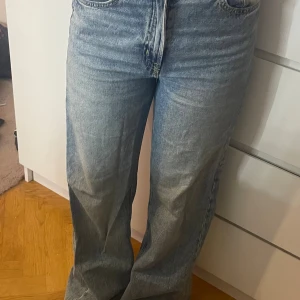 Ljusblåa raka jeans med hög midja - Säljer ett par ljusblå jeans med hög midja och raka, lite bredare ben. Klassisk femficksmodell med dragkedja och knapp framtill. Jeansen har en avslappnad passform och är tillverkade i denim. Perfekta för en chill och trendig look.💕💕pris kan diskuteras