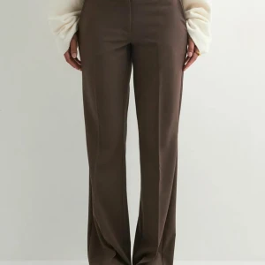 Bruna vida kostymbyxor - Snygga bruna kostymbyxor med vida ben och klassisk passform. Byxorna har hög midja och raka pressveck framtill för en clean look. Perfekta för dig som gillar stilrena och trendiga plagg. Materialet känns mjukt och följsamt. Byxorna är andvända en gång då de är lite korta för mig, är 176cm