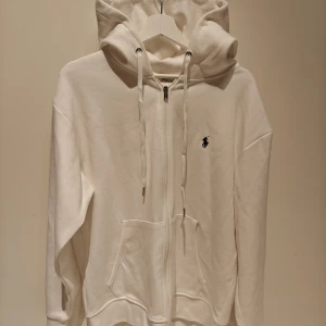 Polo Ralph Lauren Hoodie | Large | Vit - Vit hoodie från Polo Ralph Lauren med dragkedja framtill, snörning i huvan och klassisk logga broderad på bröstet. Tröjan har känguruficka och är långärmad, perfekt för en chill och stilren look. Hoodien är i storleken large & den är endast testad på så den är i ett perfekt skick. Det är en reprint i utmärkt kvalite. Skickas 1-3 dagar efter mottagen betalning. Samfraktar självklart vid behov. Har du frågor/funderingar är det bara att höra av dig! :)