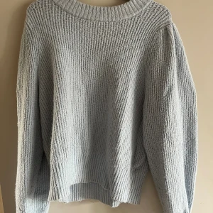 Ljusgrå stickad tröja med ribbad struktur - Mysig ljusgrå stickad tröja med bred ribbad krage och långärmad modell. Tröjan har en avslappnad passform och är perfekt för kyliga dagar. Enkel och stilren design som passar till det mesta.