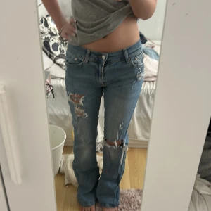 Lågmidjade slitna blå jeans - Säljer ett par ljusblå jeans med låg midja och utsvängda ben. Jeansen har flera slitningar och hål på framsidan och lite på bakfickorna. Säljer då dem är för långa och för stora för mig 💕💕de står ingen storlek men skulle säga mellan S och M