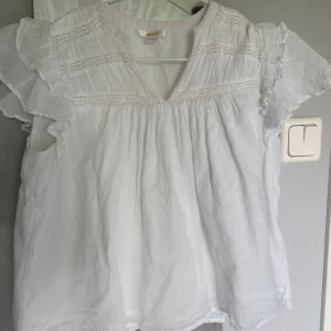 Vit blus med volang från Gina Tricot - Supersöt vit blus från Gina Tricot med volangärmar och v-ringning. Blusen har fina spetsdetaljer upptill💞 super bra skick!
