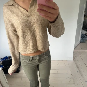 Beige stickad polotröja croppad - Beige stickad polotröja med v-ringning och krage. Tröjan är croppad och har långa ärmar samt ribbade muddar. 