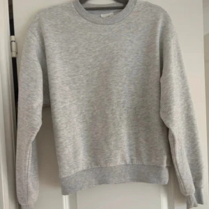 Grå sweatshirt från Basically Basics - En enkel och clean grå sweatshirt från Basically Basics i storlek S. Tröjan har rund hals, ribbade muddar vid ärmslut och nederkant, samt långärmad passform. Perfekt för chill dagar och passar till allt. Materialet är mjukt och känns skönt mot huden.
