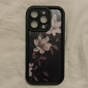 iPhone 15 Pro  - Snyggt och tåligt mobilskal för iPhone 14 Pro Max med elegant blommönster i svart och vitt. Skalet är i fint skick utan synligt slitage, ger bra skydd och har exakta utskärningar för kameror och knappar. Perfekt för dig som vill kombinera stil med funktion.