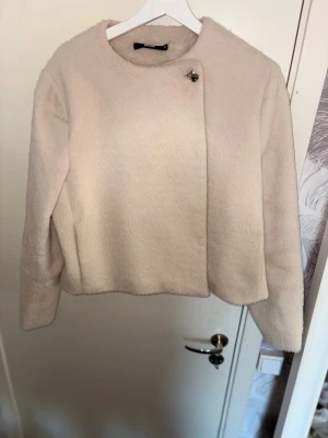 Rosa jacka från bik bok - Säljer en beige teddyjacka  i storlek M. Jackan har en rund halsringning, långärmade ärmar och en snygg metallknapp upptill. Mjuk och fluffig yta med croppad passform, perfekt för dig som gillar stilrena och mysiga plagg.