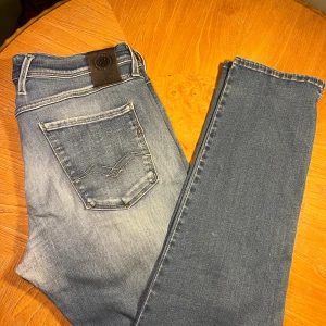 Replay Hyperflex ljusblå jeans - Säljer ett par Replay Hyperflex jeans i ljusblå tvätt med snygga slitningar och klassiska fem fickor. Jeansen har raka ben och normal passform, med stretchigt material för extra komfort. Märkespatch baktill och coola detaljer på bakfickorna. Riktigt feta jeans