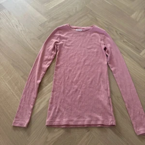 Rosa ribbad långärmad tröja XXS - Säljer en ljusrosa långärmad tröja i storlek XXS. Tröjan har en rund halsringning och är ribbad i materialet vilket ger en snygg och enkel look. Perfekt att ha som basplagg och lätt att matcha med andra kläder.