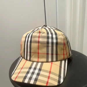 Burberry rutig keps beige M - Snygg keps från Burberry i klassiskt rutigt mönster med beige, svart, vitt och röda detaljer. Märke med 'Burberry London England' baktill. Tillverkad i bomull och polyester, perfekt för dig som vill sticka ut med en ikonisk accessoar.