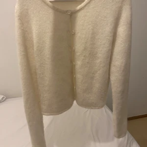 Vit kofta från Gina Tricot - Mysig vit kofta från Gina Tricot i premiumkvalitet. Koftan har rund hals, långa ärmar och knappar framtill. Materialet är stickat och känns mjukt mot huden, perfekt för att hålla värmen under kyliga dagar. Enkel och stilren design som är lätt att matcha.