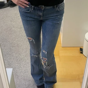 Lågmidjade jeans - Säljer ett par blå jeans från Zara i storlek 34 med snygga slitningar och hål på knäna. Modellen har bootcut