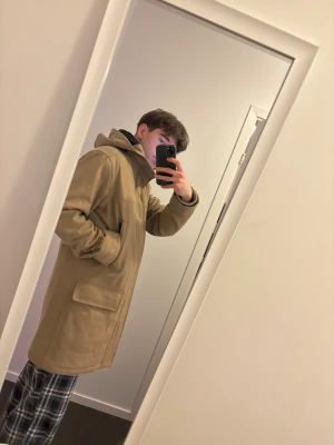 Beige parkajacka Peak Performance M - Säljer en beige parkajacka från Peak Performance i storlek M. Jackan har huva, två stora fickor med lock framtill och en stilren design. Materialet är mjukt och känns som ullmix, perfekt för kyliga dagar. Jackan är lång och har en normal passform.