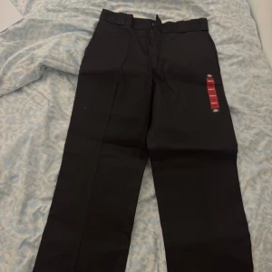 Mörk bruna Dickies 874 work pants W30/L32 - Mörkbruna Dickies 874 work pants med original fit och klassisk look. Byxorna har raka ben, bälteshällor och två bakfickor med Dickies-logga. Materialet är slitstarkt och rynkresistent polyester/bomull. Perfekt för dig som gillar streetwear och clean stil.