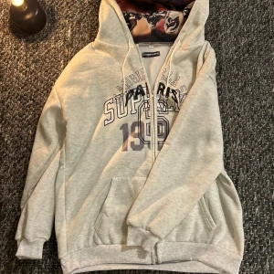 Supreme x maison margiela - Supreme hoodie i ljusgrått med coolt tryck på bröstet och årtalet 1992. Insidan av huvan har ett unikt mönster med motiv. Tröjan har snörning i huvan, känguruficka och ribbade muddar. Perfekt för dig som gillar streetwear och vill sticka ut.