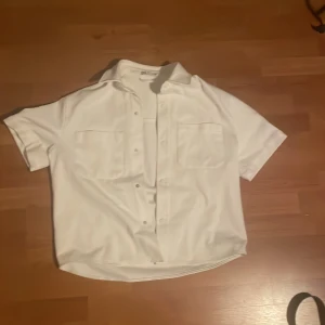 Vit overshirt från Zara - Vit overshirt med korta armar och två stora bröstfickor. Klassisk krage och knappar framtill. Skjortan har en rak passform och är tillverkad i ett mjukt tyg som känns skönt mot huden. Perfekt för en clean och stilren look. Den är is Torkel medium men den är liten så den passar mer s