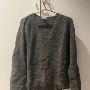 Mörkgrå stickad v-ringad tröja - Mysig mörkgrå stickad tröja med v-ringad hals och långa ärmar. 