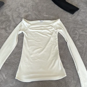Vit offshoulder topp från Amisu - Säljer en stilren vit offshoulder topp från Amisu i storlek XS. Toppen har lång ärm och är figurnära med en mjuk, stretchig känsla. Perfekt för dig som gillar minimalistisk stil och vill ha en enkel men snygg topp med smickrande passform.