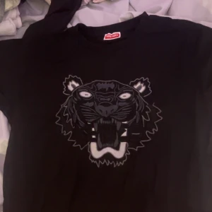 Svart Kenzo t shirt med tigertryck - Svart sweatshirt från Kenzo med ikoniskt tigertryck i grå och vita toner på bröstet. Tröjan har rund hals och lång ärm, perfekt för dig som gillar streetstyle och vill sticka ut med ett coolt motiv. Klassisk passform och mjukt material.