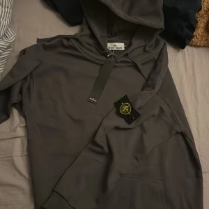 Mörkgrå hoodie från Stone Island XL - Säljer en mörkgrå hoodie från Stone Island i storlek XL. Tröjan har klassisk huva, känguruficka och den ikoniska Stone Island-patchen på ärmen. Materialet är mjukt och skönt, perfekt för chill dagar. Stilsäker och enkel att matcha med jeans eller joggers.