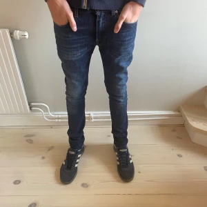 Acne Studios Thin Spaniel Vint jeans - Snygga mörkblå jeans från Acne Studios, modell Thin Spaniel Vint. De har en slim passform med klassisk femficksdesign och dragkedja. Materialet är 99% bomull och 1% elastan för skön stretch. Perfekta för dig som gillar stilrena och moderna jeans.
