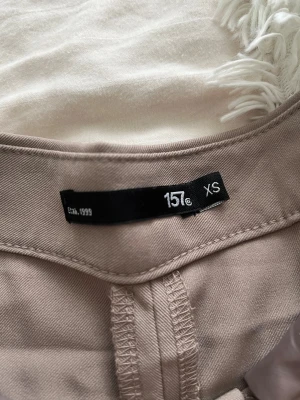 Beige wide kostymbyxor från 157 XS.  - Snygga beige kostymbyxor från 157 i storlek XS. Byxorna har ett wide fit med raka ben och klassisk midja. Perfekt för dig som gillar en clean och stilren look. Materialet känns mjukt och har en lätt struktur, vilket gör dem sköna att bära hela dagen.