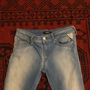 Replay ljusblå jeans - Säljer ett par ljusblå skinny jeans från Replay med klassisk femficksdesign och vita detaljer på bakfickan. Jeansen har en snygg tvätt med slitningar framtill och smal passform som sitter tajt längs benen. Perfekt för dig som gillar en modern och stilren look.