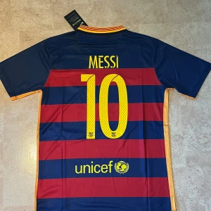 Barcelona Messi 10 fotbollströja Nike - Säljer en officiell FC Barcelona matchtröja från Nike med Messi och nummer 10 på ryggen. Tröjan har breda röda och marinblå ränder, gula detaljer och klubbmärke på bröstet. Materialet är lätt och andas, perfekt för fotboll. Sponsorer: Qatar Airways och UNICEF.