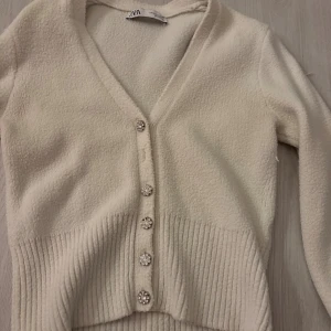 Vit kofta med pärlknappar från Zara - Superfin vit kofta från Zara med glittrande pärlknappar och v-ringad hals. En knappt borta 
