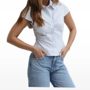 Blåvit randig skjorta med kort ärm - Snygg blåvit randig skjorta från Gina Tricot med korta ärmar och klassisk krage. Skjortan har figurnära passform, knappar framtill och lätt rynkdetalj vid bysten. Perfekt till jeans för en fräsch look.