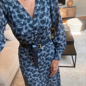 Michael kors Marinblå långklänning med bälte - Snygg långklänning från Michael Kors i marinblått med vitt blommigt mönster. Klänningen har v-ringning, långa ärmar och ett matchande marinblått bälte med guldfärgat spänne i midjan. Perfekt för dig som gillar stilrena detaljer och mönster.