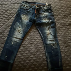 Replay Anbass jeans med slitningar - Säljer ett par mörkblå Replay Anbass jeans med coola slitningar och färgstänk på framsidan. Jeansen har fem fickor, knapp och dragkedja i midjan samt skinny passform. Perfekt för dig som gillar en edgy streetstil.