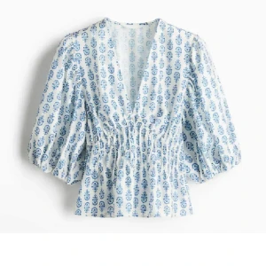 Vit och blå blus med puffärm - Supersöt blus i vitt med blått blommönster, djup v-ringning och smockad midja. Puffiga trekvartsärmar ger en trendig siluett. Perfekt till jeans eller kjol för en fräsch look. Knappt använd och superbra skick, storlek M men ganska liten i storleken, funkar för mig som brukar ha xs, men en aning stor💙