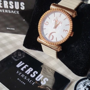 VERSACE damklocka i roseguld med box, papper & nytt batteri - Stilren elegant klocka från Versace(2200kr+ i butik) med rund urtavla i vitt och detaljer i roséguld.  Bytt batteri och blivit servad inför försäljning så kommer gå 2-5år utan problem. Urtavlan har ett solstrålemönster och stora siffror vid 3, 6 och 9. Armbandet är beige och har en diskret räfflad struktur. Perfekt accessoar för dig som gillar lyxig design.