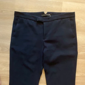 Svarta bootcut kostymbyxor Divin Woman - Svarta kostymbyxor från Divin Woman med bootcut-ben och klassisk passform. Byxorna har hög midja, snedställda fickor fram och dekorfickor bak. Snyggt skräddade i ett mjukt tyg som ger en dressad look. Finns ett hål i linningen men syns inte när byxorna är stängda . Mycket bra skick 