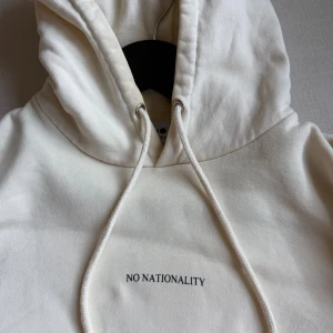 Beige hoodie från NN07 - Säljer en stilren ljusbeige hoodie från NN07 med broderad text på bröstet. Tröjan har huva med snörning, känguruficka och långa ärmar. Mycket fint skick. Storlek S men passar även lite mindre M.