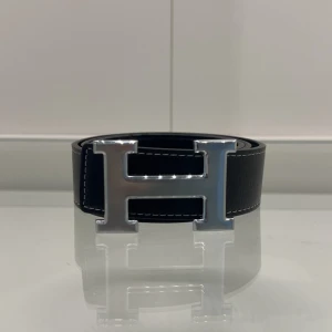 Svart snyggt bälte med silver H-spänne - Perfekt accessoar för att lyfta vilken outfit som helst.