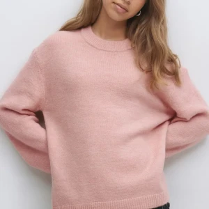 Ljusrosa stickad tröja - Supermysig ljusrosa stickad tröja med rund halsringning och långa ärmar. Tröjan har en relaxed passform och ribbade muddar vid ärmslut och nederkant. Perfekt för lager-på-lager under kyliga dagar.