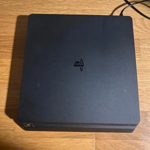 PlayStation 4 Slim - Sony PlayStation 4 Slim i svart färg. Konsolen är i gott skick med mindre tecken på normalt bruk. Kompakt design, HDMI, USB och nätverksport synliga. Perfekt för gaming och streaming. Inga synliga större defekter eller repor. Alla kablar och laddare till den ingår och kan även slänga in en kontroll på köpet, dock så fungerar kontrollen inte särkilt bra.