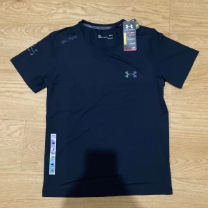 Under armour tshirt (helt ny+gratis frakt) - Svart t-shirt från Under Armour med HeatGear-teknologi. T-shirten har korta ärmar, rund halsringning och ett holografiskt Under Armour-logga på bröstet samt en holografisk detalj längs sidan. Perfekt för dig som gillar sportig och clean stil.