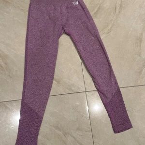 Lila seamless leggings från RW - Snygga lila seamless leggings från RW med diskret mönstrad struktur vid vaderna och längs sidorna. Hög midja och tight passform, perfekta för träning eller chill. Stretchigt material som sitter skönt och följer kroppen.