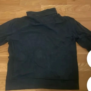Mörkgrå half zip tröja från Polo Ralph Lauren - Mörkgrå långärmad tröja från Polo Ralph Lauren med klassisk half zip och hög krage. Tröjan har en broderad logga på bröstet och är tillverkad i mjuk bomull. Perfekt för lager-på-lager och chill stil.