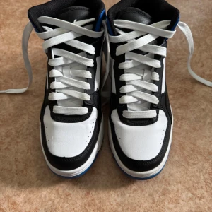 Puma sneakers svart/vit/blå strl 38 - Puma sneakers i svart, vitt och blått i storlek 38. Skorna har snörning, platt blå sula och rund tå. Skorna är normala i storlek och har bara använts ett par gånger. 