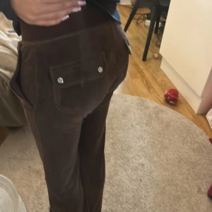 Bruna mjukisbyxor Juicy Couture XXS - Bruna mjukisbyxor från Juicy Couture i supermjuk velour med snörning i midjan och stora fickor med knappar bak. Klassisk relaxed fit och ikonisk 2000-talsstil, perfekta för en chill och trendig look. Dom är i bra skick ordinarie pris kan vara från 800-1200kr