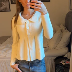 Vit kofta med stora knappar och krage - Supersöt vit kofta med stora dekorativa knappar framtill och en bred, rundad krage. Modellen är lätt utsvängd nedtill och har lång ärm. Perfekt att styla med jeans eller kjol!!🤍
