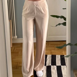 Beiga kostymbyxor  - Snygga beiga kostymbyxor från NLY Trend i storlek 36. Byxorna har hög midja, raka ben och stängs med dragkedja fram. Tillverkade i ett mjukt, lätt material som ger en clean och stilren look. Perfekta för dig som gillar en klassisk och trendig vibe.