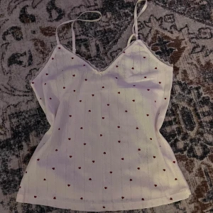 Pyjamas linne  - Supersöt vit linnetopp med tunna axelband och små röda hjärtan över hela tyget. Toppen har v-ringning med spetskant och är perfekt för en söt och romantisk look.