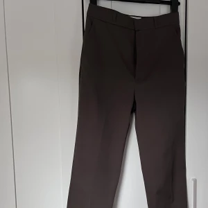 Bruna kostymbyxor med raka ben - Snygga mörkgröna(haki) kostymbyxor med klassisk rak passform och pressveck. Byxorna har hällor för bälte och sidofickor, perfekta för en stilren look. Materialet känns slätt och dressat.