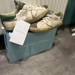 Philippe Model vita sneakers med gröna detaljer - Säljer ett par snygga Philippe Model sneakers i vitt skinn med gröna detaljer och gråa partier. Klassisk låg modell med snörning och rund tå. Skorna har en cool vintage-look och är perfekta för dig som gillar streetstyle. Levereras med originalkartong och tag.    Följarna Fuck bästäma pris så därför så billigt🔥. Dom e köpta på Merch Sweden för ett halvår sedan. 